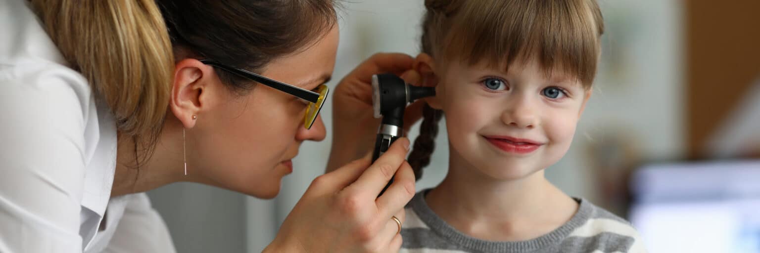 Pediatrician examines ear of sick child in office of hospital background. Otitis Prevention Concept